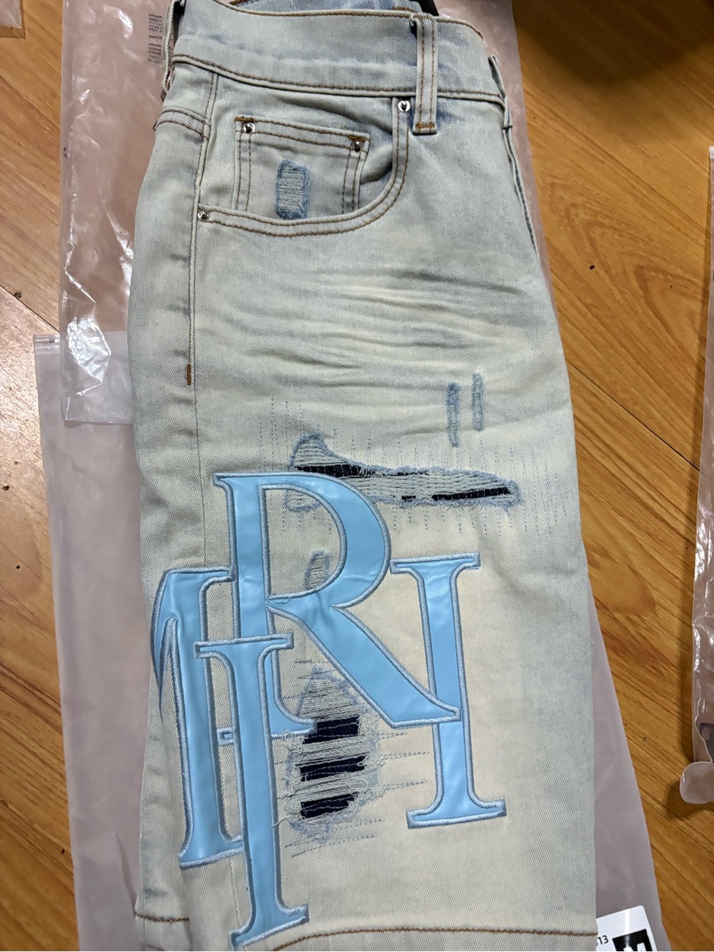 AMIRI Light Blue Distressed Men’s Jean Shorts with Large Patch Initials